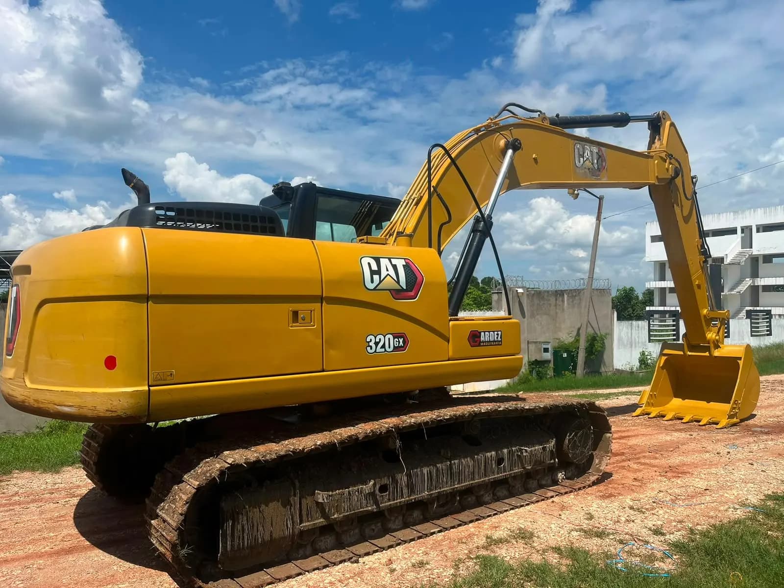 Excavadora de orugas CAT 320 GX de lado, con el cucharón apoyado en el suelo.